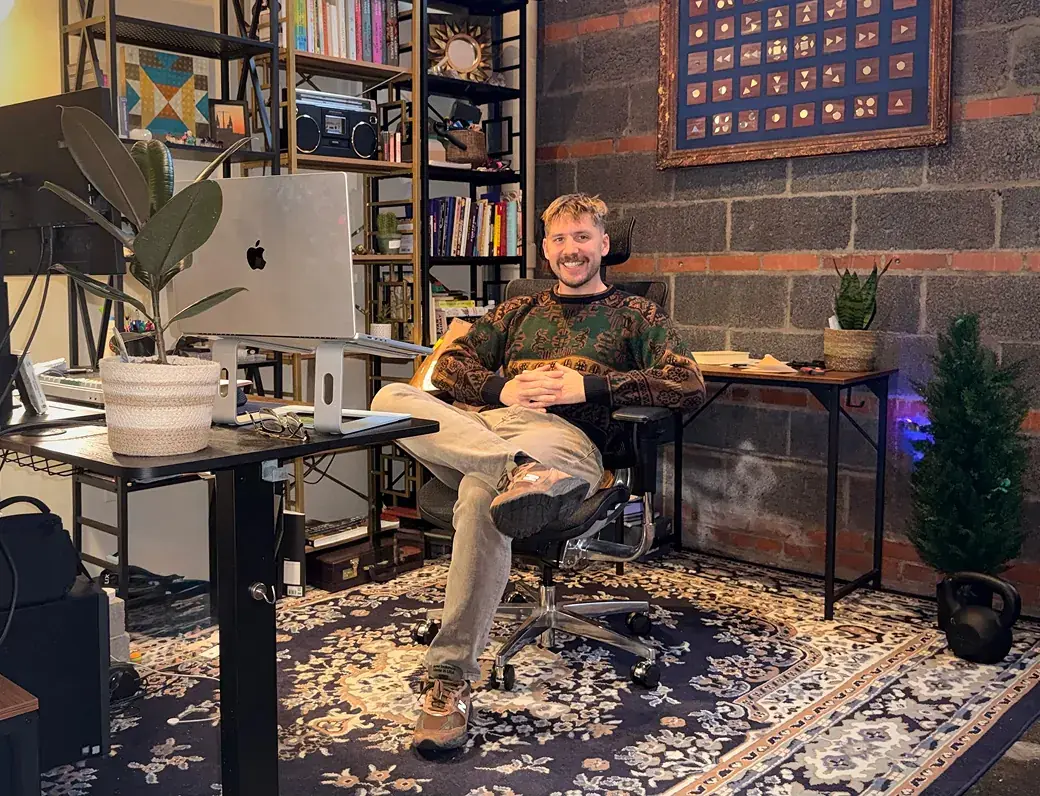 Luc Gensler sitting at his desk in a home studio with bookshelves and a brick wall